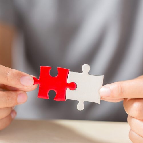 hand connecting two puzzle pieces on table background, business strategy concept
